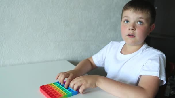 Junge spielt mit Pop it sensorischem Spielzeug. Junge drückt auf bunte regenbogensquishy weiche Silikonblasen. — Stockvideo