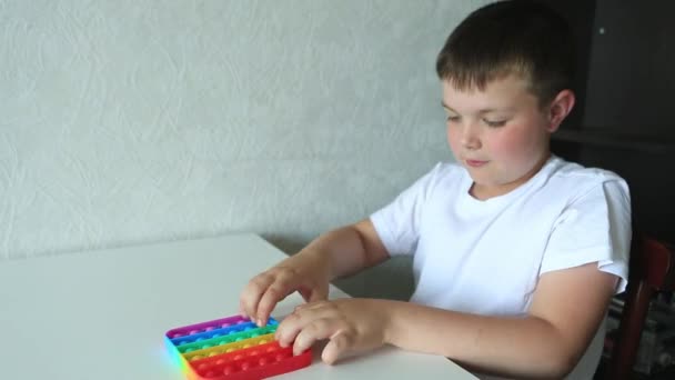 Menino brincando com pop-lo brinquedo sensorial. Menino pressiona no arco-íris colorido squishy bolhas de silicone macio. — Vídeo de Stock