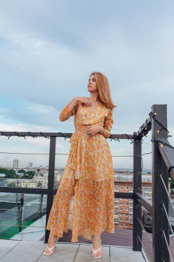 Uzun leopar desenli elbiseli güzel bir kadın bir binanın çatısında merdivenlerde dikiliyor..