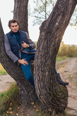 Sarı sonbahar ormanında ağacın yanında duran uzun boylu yakışıklı adam.