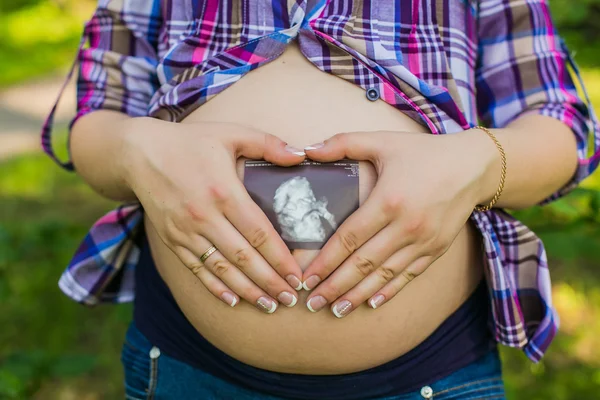 Schwangere im Park macht Herzzeichen am Bauch — Stockfoto