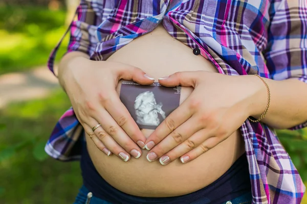 Mulher grávida no parque fazendo sinal de coração na barriga — Fotografia de Stock