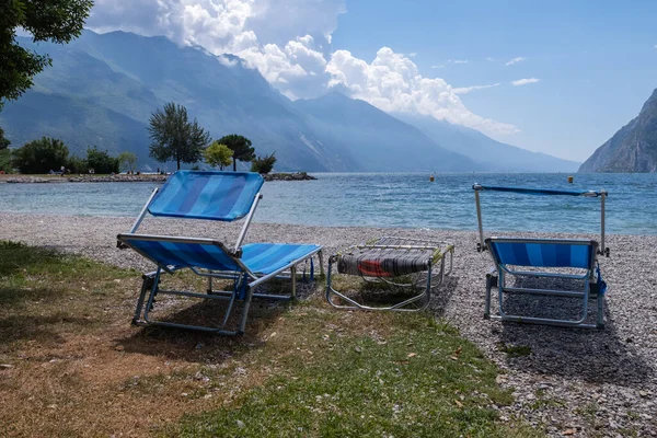 Göl ve dağ manzaralı boş şezlonglar, Riva del Garda 'da taş plaj.