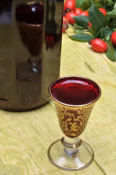 En flaska sprit, glas och nypon frukt — Stockfoto