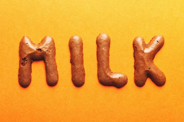 Milk一词来自橙色背景的饼干 — 图库照片