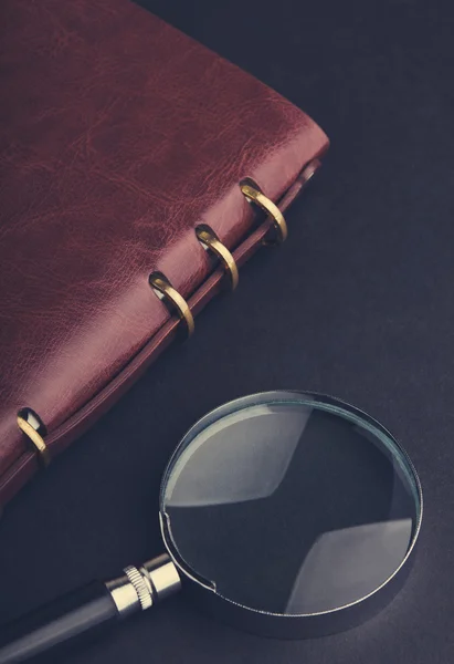 Notebook with a magnifier on black — Stock Photo, Image