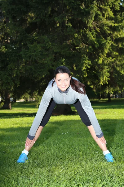 Smiling woman stretching in the park — Stock Photo, Image