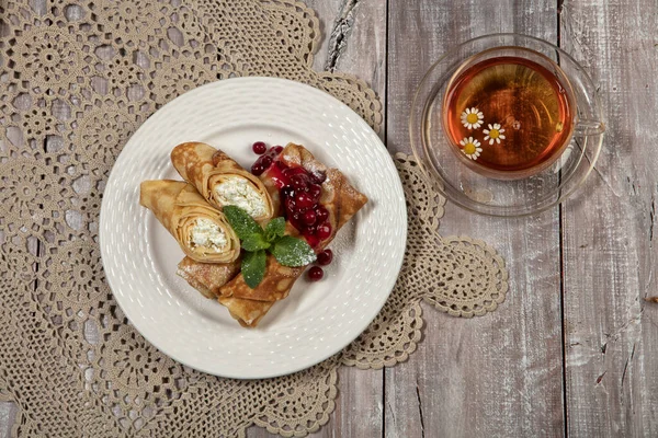 Plate with pancakes with meat and cup of tea on an old wooden background