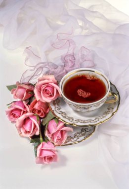 Kumaş arka planda bir fincan çay ve çiçek.