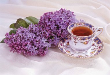 Kumaş arka planda bir fincan çay ve çiçek.