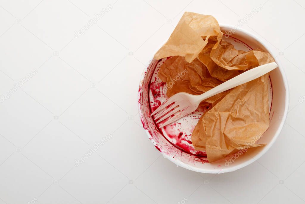 Dirty disposable bowl and fork after eating on a white background