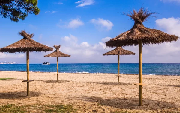 Playa solitaria, sombrillas de paja, mar, cielo azul y lancha rápida turística . — Foto de Stock