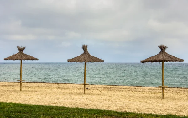 Tres sombrillas de paja en la playa de arena . — Foto de Stock