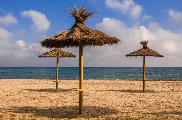 Tres sombrillas de paja en la playa de arena . — Foto de Stock