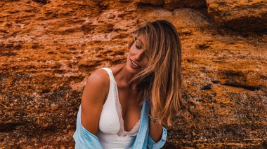 Beyaz elbiseli ve kot gömlekli çekici kız Sandy Rock 'ın yanında poz veriyor. 