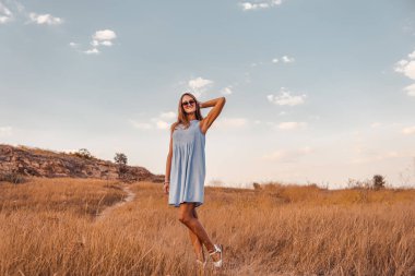 Yazlık elbiseli, güneş gözlüklü mutlu genç kadın çayırda poz veriyor. 