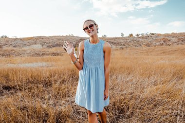 Yazlık elbiseli, güneş gözlüklü mutlu genç kadın çayırda poz veriyor. 