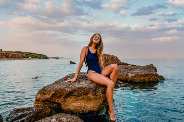 坐在海水潮湿的卵石上 身穿运动服的迷人的晒黑了的年轻女子摆出一副姿势 — 图库照片