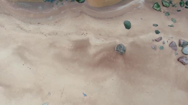 Vista aérea de arriba hacia abajo desde el dron de olas de mar tranquilas estrellándose y espumando sobre piedras de roca en la playa de arena — Vídeos de Stock
