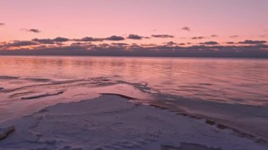 Donmuş deniz kıyısında sakin bir denizde gün batımı.