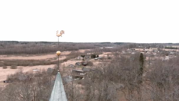 Kleine Dorfkirche mit goldenem Wetterfahnenhahn auf dem Kirchturm in Umurga, Lettland. Luftaufnahme von der Drohne — Stockvideo