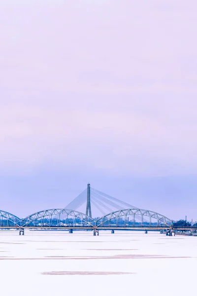 Riga cityline with bridges over frozen river Daugava — Stock Photo, Image