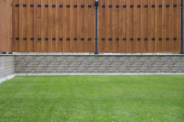 Valla de madera con piedra de hierba básica y verde en frente . Imagen de archivo