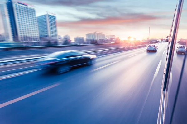 Bilkörning på motorväg vid solnedgången, rörelse suddig — Stockfoto