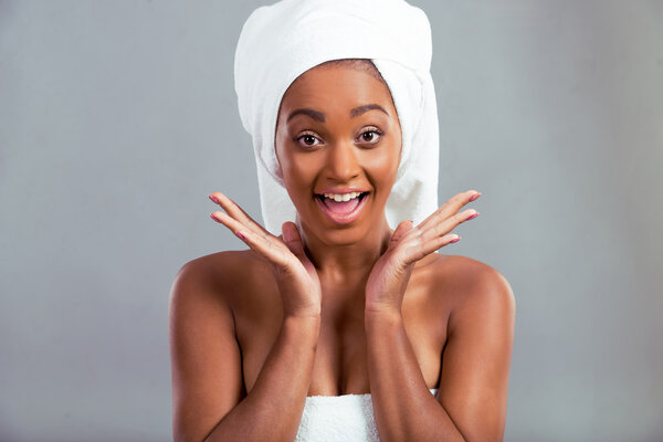 Happy beautiful Afro American girl with a towel on her head is looking at camera and smiling, on a gray background