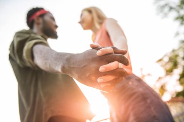 Koyu tenli bir adamla sarışın bir kadının bir caddede yürürken el ele tutuşup gülümsedikleri neşeli genç bir çift.