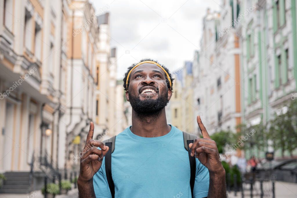 A young black man rejoices raising his fingers up while walking the streets of the bridge with a backpack