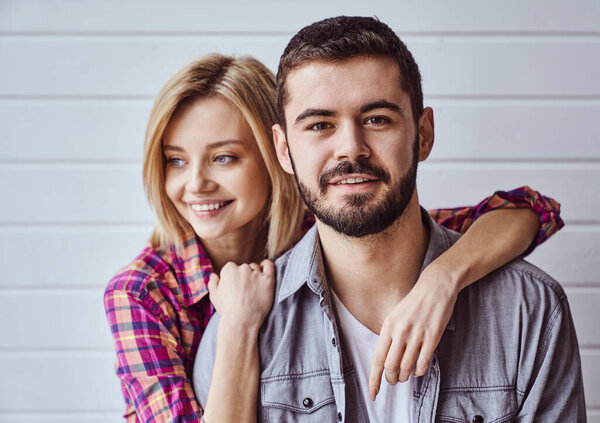Портрет молодой веселой любящей пары, улыбающейся в камеру и обнимающей друг друга на светлом фоне