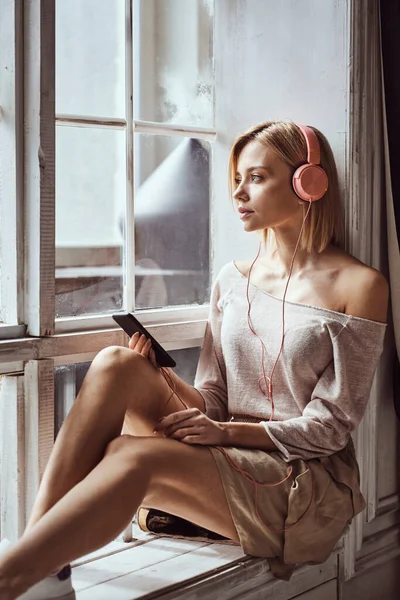 Joven Chica Hermosa Sentada Alféizar Ventana Escuchando Música Auriculares Rosados — Foto de Stock