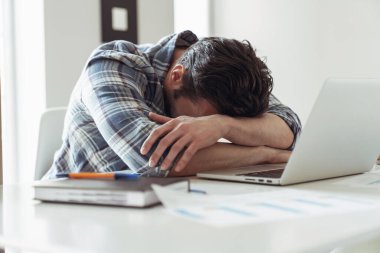 Genç bir erkek işadamı dizüstü bilgisayarla çalışırken mutfakta masada oturup çalışırken uyuyakalıyor.