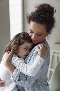 İyi bir aile, anne ve kız. Küçük kız, gülümseyerek annesine sarılıyor ve gözleri kapalı evde.