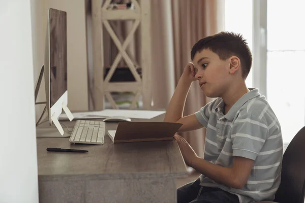 Mały Chłopiec Siedzi Swoim Pokoju Przy Biurku Obok Komputera Odrabia — Zdjęcie stockowe
