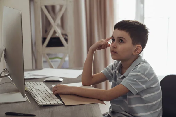Mały Chłopiec Siedzi Swoim Pokoju Przy Biurku Obok Komputera Odrabia — Zdjęcie stockowe