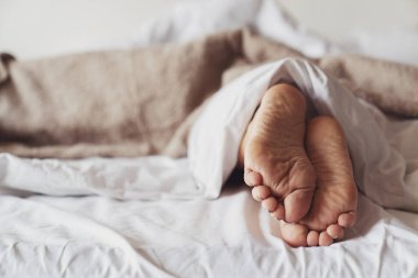 Yatak odasındaki battaniyenin altından sarkan kadın bacakları. Kadın yorgun, uyuyor ve uyanamıyor..