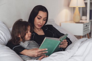 İyi geceler. Genç ve güzel bir anne küçük kızını yatağa yatırır ve geceleri ona çocuk hikayeleri kitabı okur..