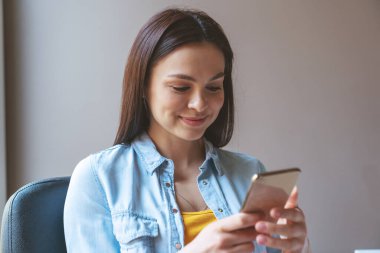 Evinde ya da iş yerinde otururken telefonunu kullanan genç ve serbest bir kızın portresi..