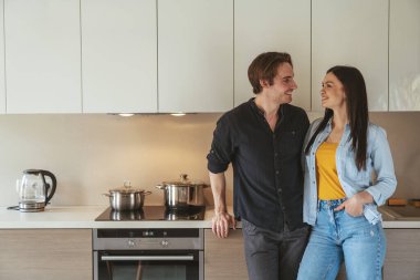 Genç ve neşeli bir çiftin portresi. Evde, mutfakta durmuş, bir şeyleri tartışıyorlar..