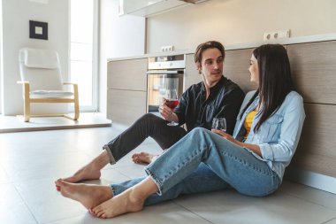 Genç ve neşeli bir çiftin portresi. Evde, mutfakta yerde oturmuş kadehten şarap içip bir şeyler tartışırken eğleniyorlar..