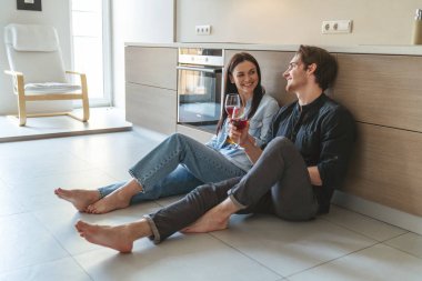 Genç ve neşeli bir çiftin portresi. Evde, mutfakta yerde oturmuş kadehten şarap içip bir şeyler tartışırken eğleniyorlar..