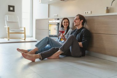 Genç ve neşeli bir çiftin portresi. Evde, mutfakta yerde oturmuş kadehten şarap içip bir şeyler tartışırken eğleniyorlar..