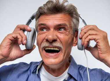 Kulaklık takan ve müzik dinlerken duygusal tepki veren neşeli orta yaşlı bir adamın yakın plan portresi. Zevk kavramı, ses deneyimi, yaşam tarzı ve ses eğlencesi.
