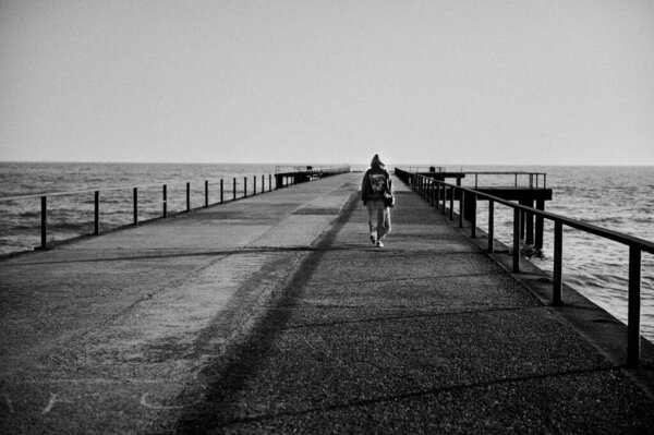 черно-белое фото девушки, идущей вдоль пирса вдали от Черного моря на вечерней горизонтальной фотографии