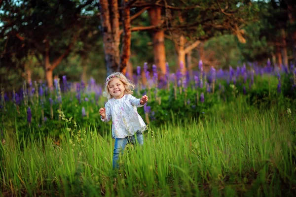 Menina bonita com flores azuis no campo. Luz do sol. Cabelo loiro . — Fotografia de Stock