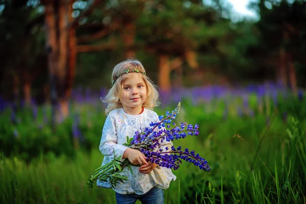 Vacker liten flicka med blå blommor på fältet. Sunshine. Blont hår. — Stockfoto