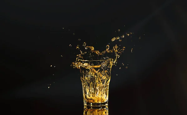 黒い背景の上に氷のキューブからのスプラッシュを持つウイスキーのガラス アルコールが飛び散った ウィスキーやコニャックやその他のアルコールの一種で — ストック写真