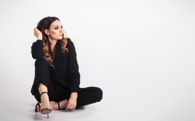 Gri arka planda oturan zarif bir iş kadını.